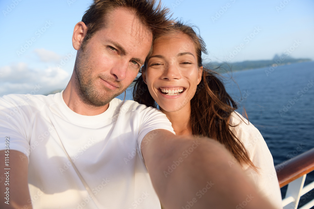 Selfie couple taking holiday self-portrait picture of themselves. Happy multiracial friends having fun together on cruise vacation in Caribbean destination taking smartphone photos as summer memories.