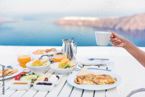 Morning person drinking coffee cup at breakfast table with mediterranean sea view. Woman eating at restaurant outside terrace patio on Santorini, Greece, Europe destination summer vacation.
