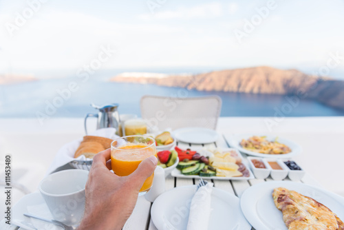 European vacation healthy breakfast food selfie. POV of man drinking morning orange juice at resort restaurant. Table for two on outdoor hotel balcony caldera view on Oia Santorini, Greece, Europe.