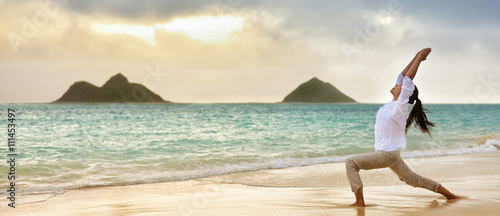 Yoga woman meditating in warrior I pose at hawaiian beach during beautiful morning sunrise against Lanikai's mountains Hawaii landmark . Banner panoramic crop for advertisement. photo