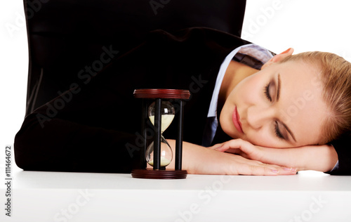 Young business woman sleeping on the desk with hourglass photo