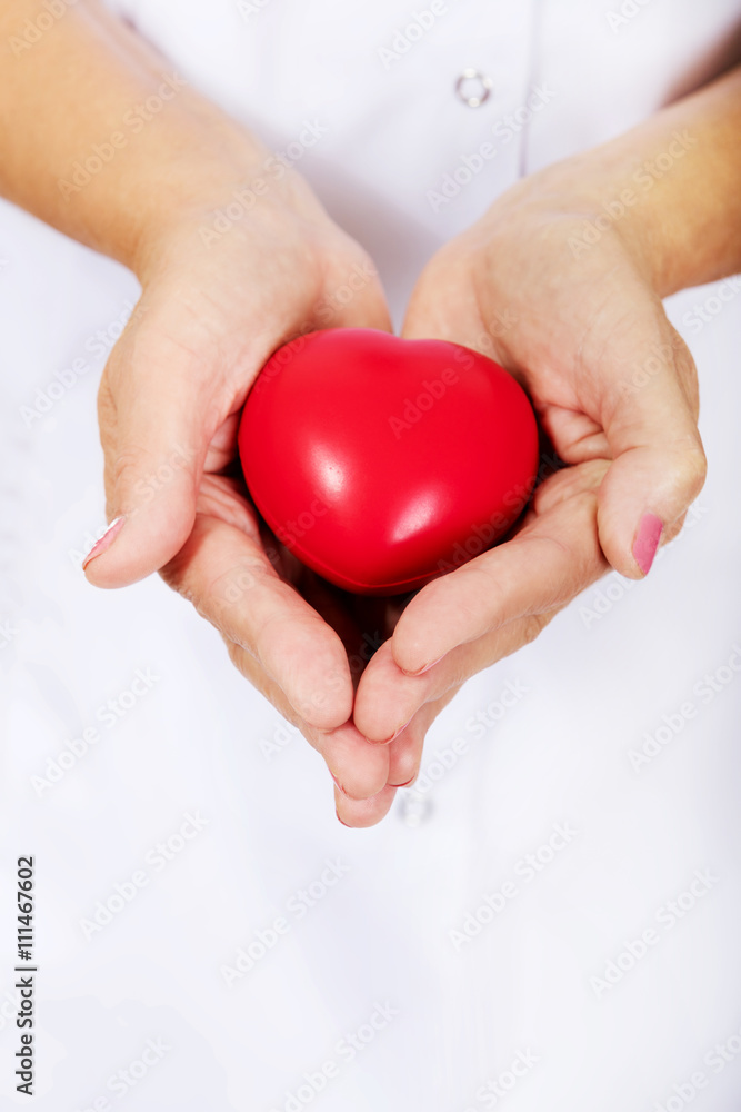 Elderly female doctor or nurse holding red toy heart Elderly female doctor or nurse holding red toy heart