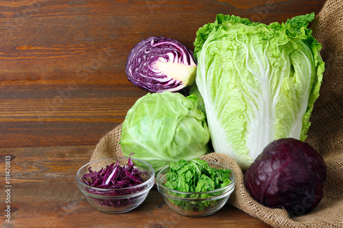 different types of cabbage near the glass bowl on sackcloth on wooden brown background