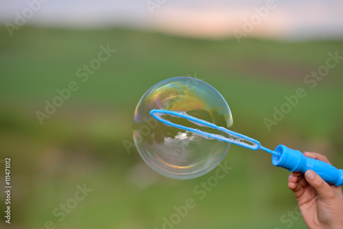 Close up of a soap bubble growing from the blower ring hold by a photo