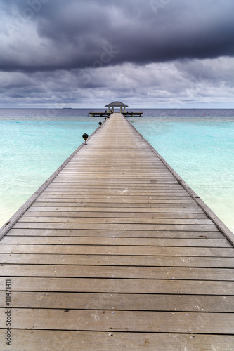 Wooden jetty over the beautiful Maldivian ocean with blue sky