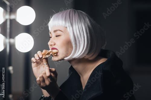 Funny woman in blonde wig eating pizza in dressing room
