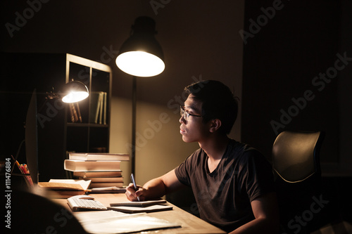 Concentrated man using computer for studying and writing in notepad