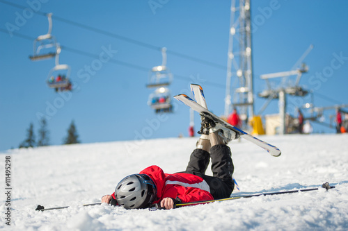 Skier lying face in the snow at mountain top in sunny day with ski lifts and blue sky in background