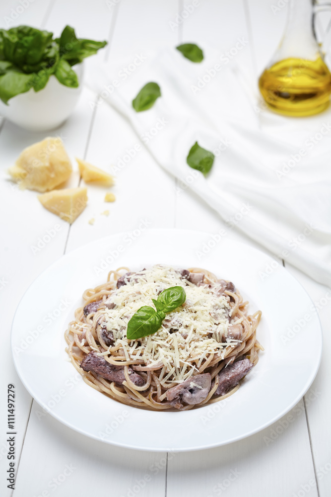 Traditional Italian spaghetti pasta with roasted beef, champignon mushrooms, parmesan cheese and basil. Restaurant menu meal in white plate
