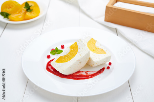 Panna cotta souffle sweet dessert with peach and berry sauce in white plate. Delicious restaurant milk pudding meal.