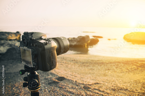 Photo camera on a tripod. Photographing sunrise on the sea shore