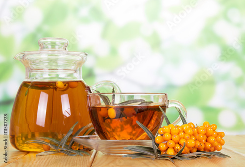 Jug, cup tea with sea-buckthorn berries on  green abstract. photo