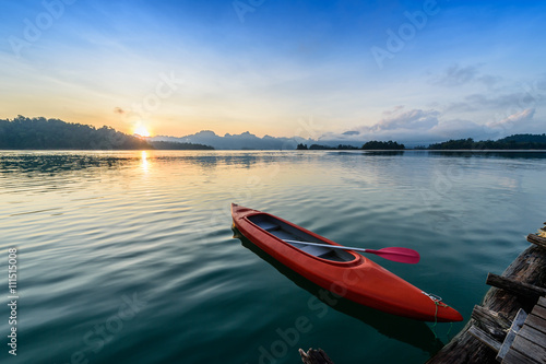 Canoe floating on the calm water under amazing sunrise