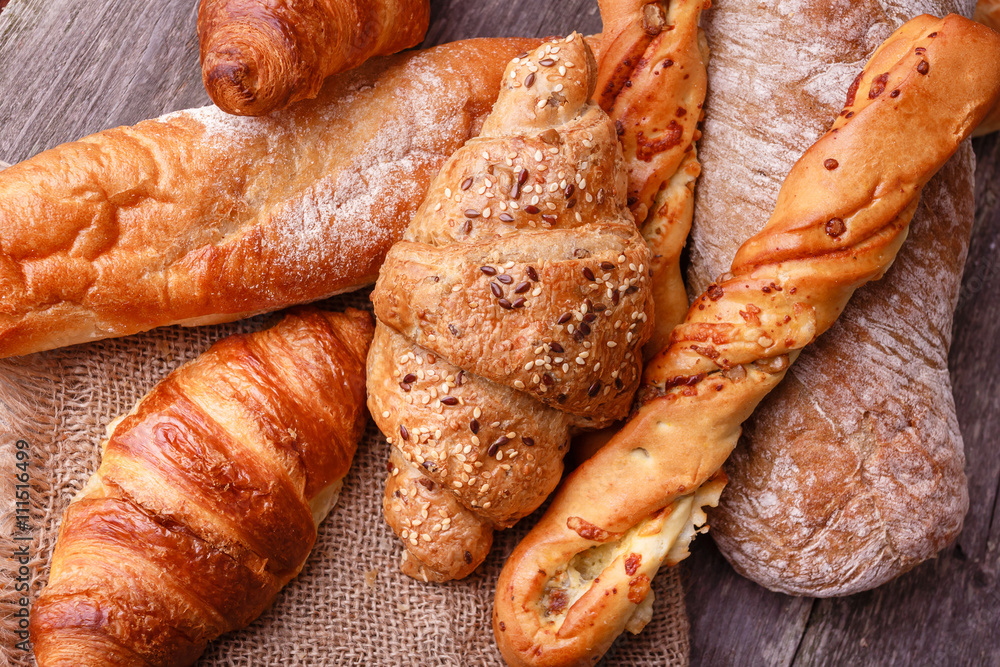 Assortment of fresh baked bread and croissants on burlap on rustic table Assortment of fresh baked bread and croissants on burlap on rustic table