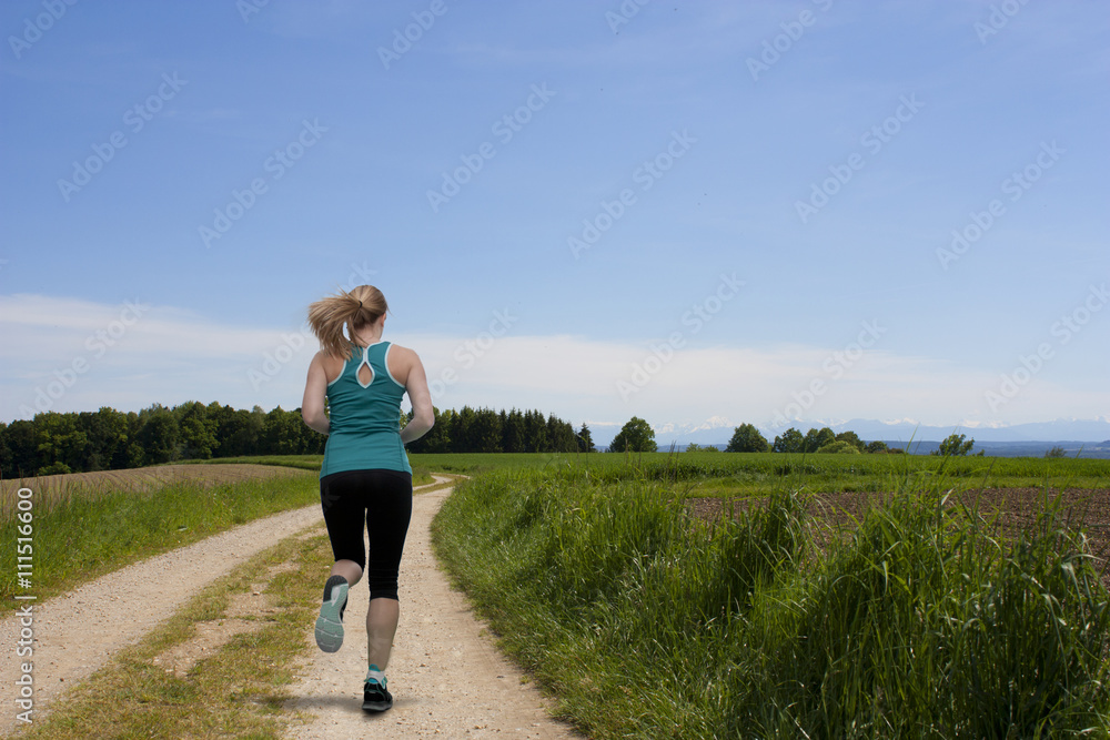 Frau läuft auf einem Weg neben einem Feld dem Ziel entgegen Frau läuft auf einem Weg neben einem Feld dem Ziel entgegen
