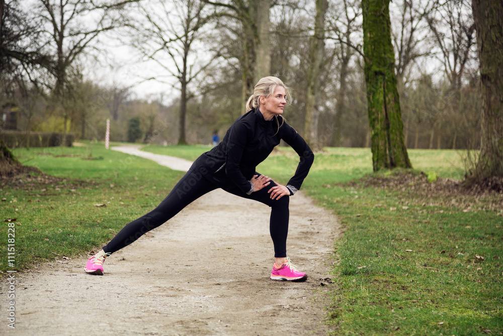 Fototapeta premium woman stretching her legs in the park before having a run. Cold winter day with sport activity