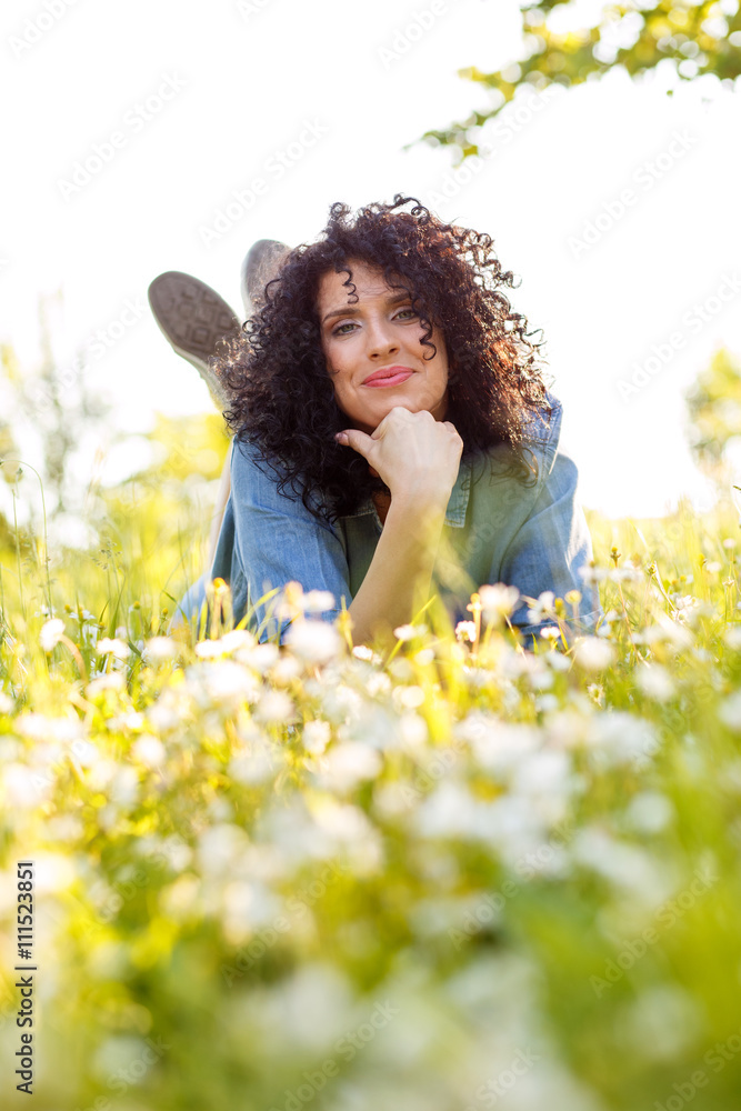 Beautiful young woman laying on a green grass in a park with white flowers around her. Beautiful young woman laying on a green grass in a park with white flowers around her.