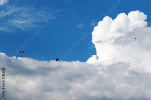 Parachutists are flying in the cloudy sky © Gribanov