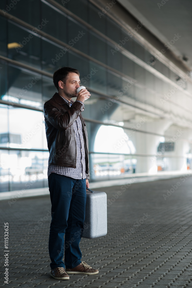 Young handsome man with coffee cup and suitcase in the airport