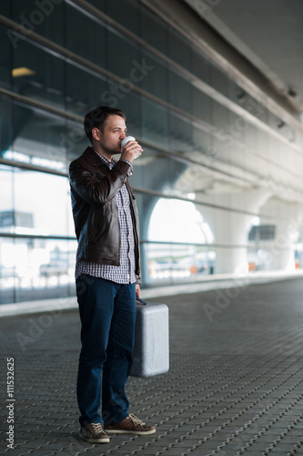 Young handsome man with coffee cup and suitcase in the airport