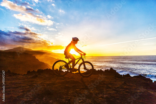 Mountain biking MTB cyclist woman cycling on bike trail on coast at sunset. Person on bike by sea in sportswear with bicycle enjoying healthy active lifestyle in beautiful nature.