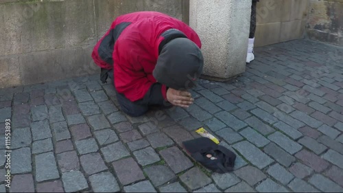 Dolly shot of beggar drifter on streets praying for money a passer by giving coins throwing them in hat laying on old street man kneeling forward does prayer when gets cash stabilized 4k resolution photo