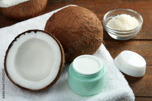 halves of coconut with an open jar of cream and coconut in glss bowl on a towel on a wooden brown background