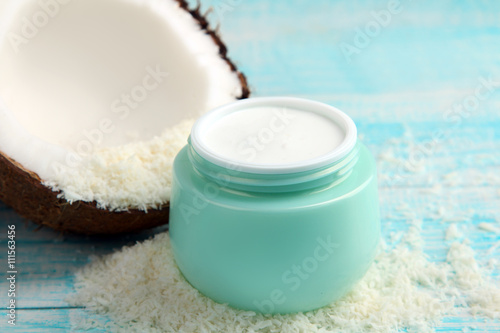 halves of coconut with an open jar of cream and coconut on wooden blue background