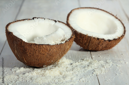 cut coconut with coconut flakes on white wood background
