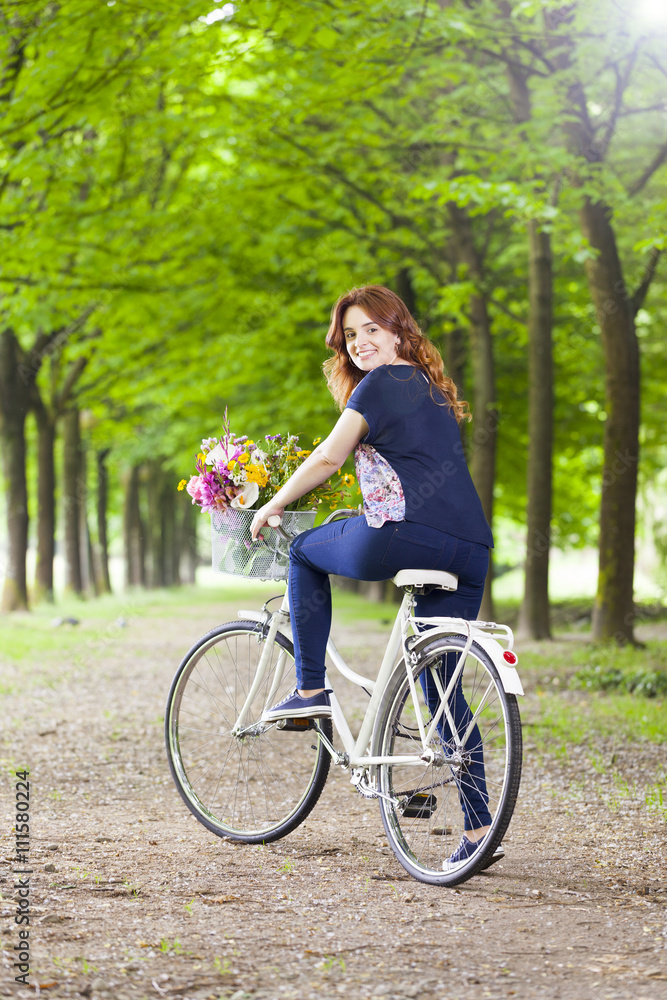 Fototapeta premium Beautiful young woman standing with a vintage bicycle at the par