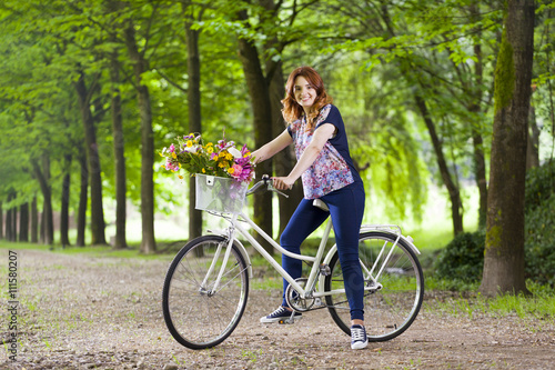 Beautiful young woman standing with a vintage bicycle at the par