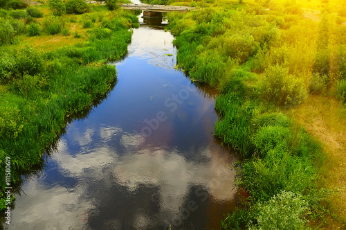 River view from above.. reflected in water blue sky and clouds in the distance on the background is the old bridge. bushes and grass on the beach. warm light of the setting sun. Summer day. 