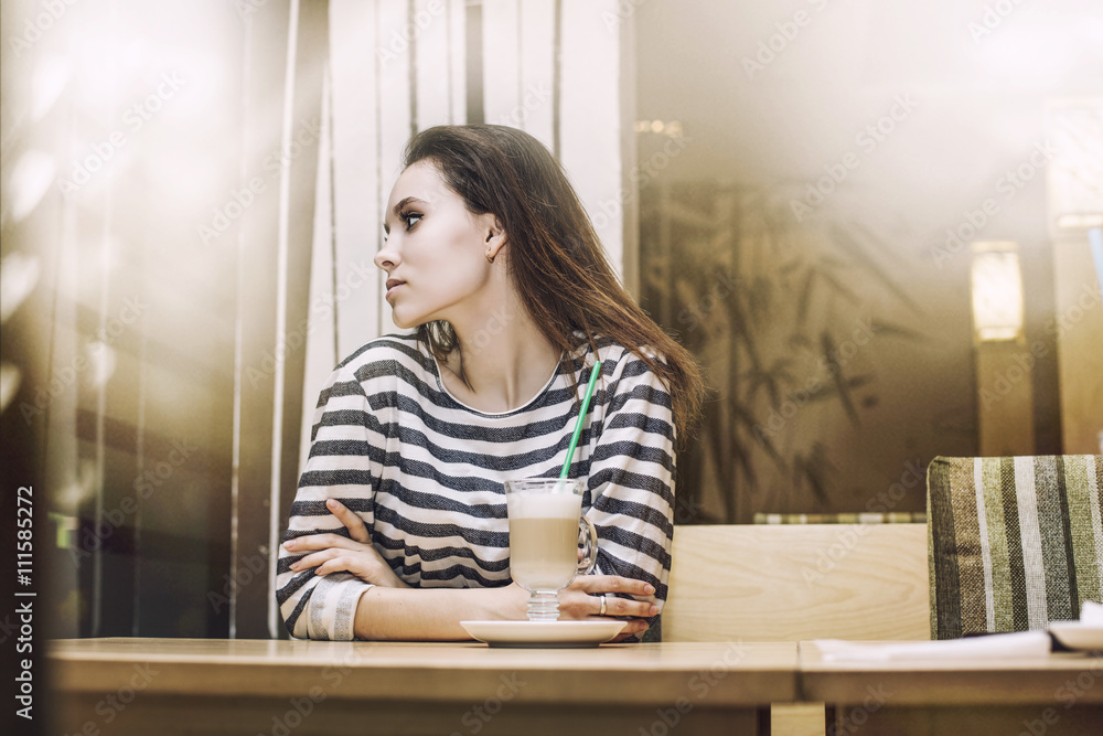 Young beautiful woman drinking latte in the coffee shop at a tab Young beautiful woman drinking latte in the coffee shop at a tab
