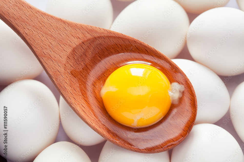 Egg yolk in wooden spoon on eggs - obrazy, fototapety, plakaty 