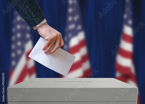 Election in United States of America. Voter holds envelope in hand above vote ballot. USA flags in background. Democracy concept.