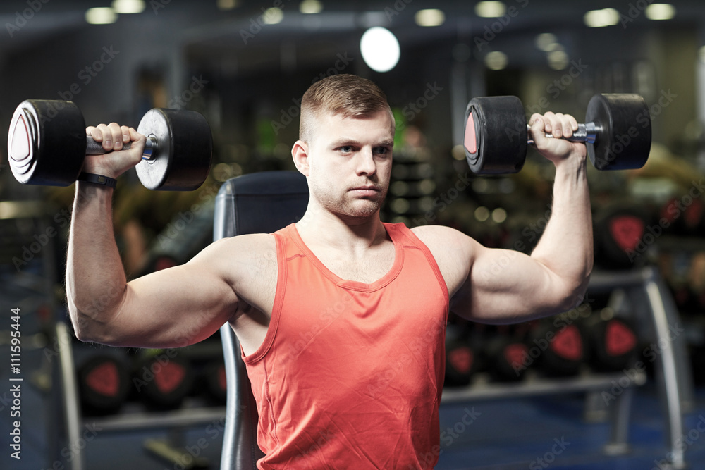 young man with dumbbells flexing muscles in gym