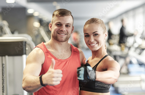 smiling man and woman showing thumbs up in gym