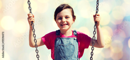 happy little girl swinging on swing over lights