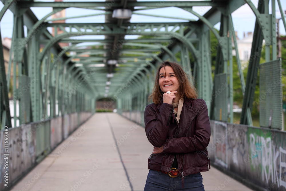 Beautiful brunette woman with leather jacket sitting on a bridge with graffiti