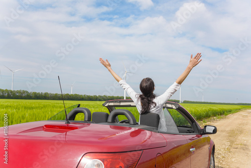 Woman in a red cabriolet in a field with wind power.
