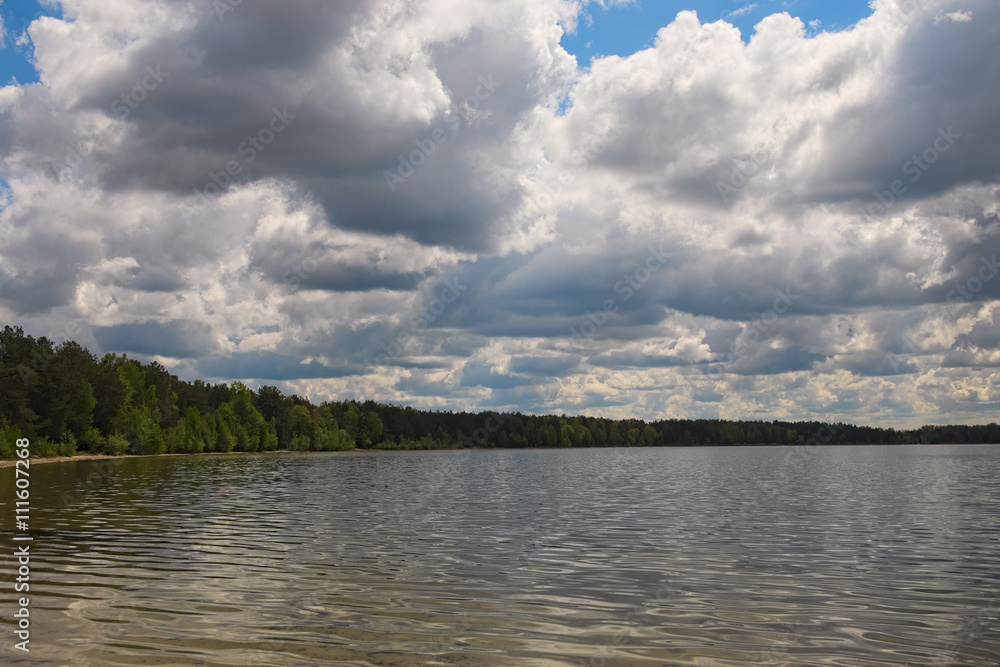 Scenic lake and forest.White clouds of different shapes are closing blue sky and sun (Pisochne ozero, Ukraine)