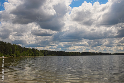 Scenic lake and forest.White clouds of different shapes are closing blue sky and sun (Pisochne ozero, Ukraine)