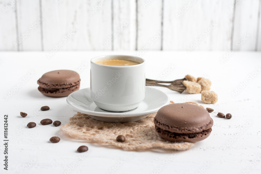 Coffee Cup and chocolate French macaroons on a white wooden back Coffee Cup and chocolate French macaroons on a white wooden back