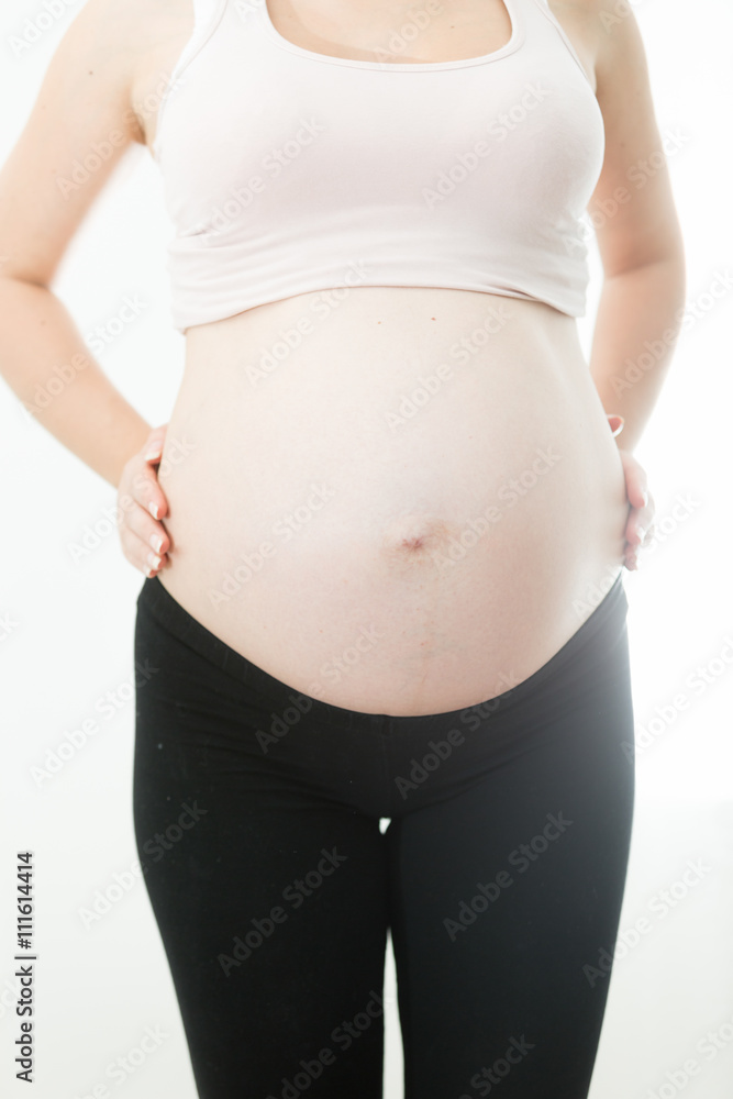 Closeup of young pregnant woman in sportswear posing on white ba Closeup of young pregnant woman in sportswear posing on white ba
