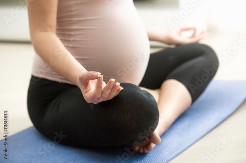 Closeup of pregnant woman meditating on floor at living room
