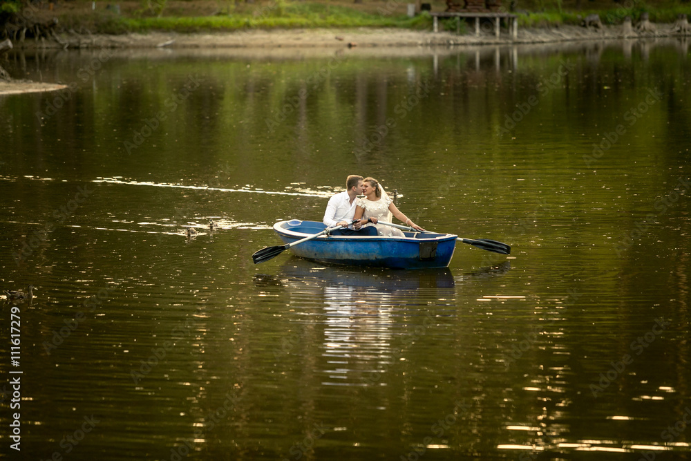 Newly married couple kissing on rowing boat in the middle of lak