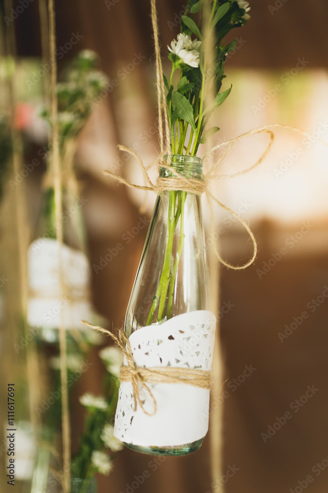 Closeup of decorative bottles with flowers hanging on ropes