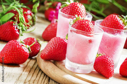 Pink granita with strawberries in a glass, old wooden background