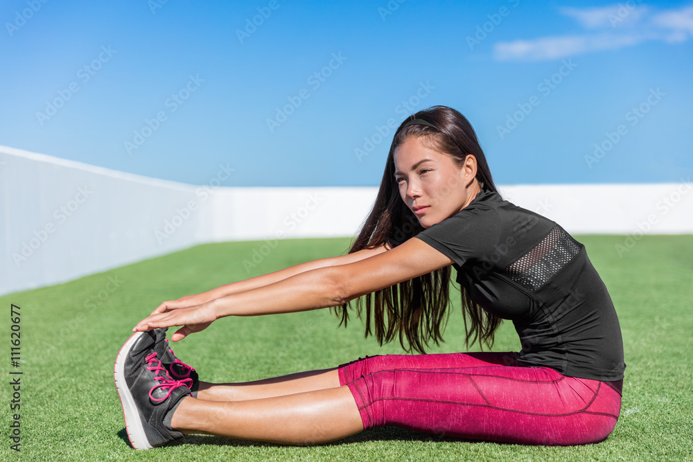 Fitness woman stretching hamstring leg muscles - back stretch sitting toe  touch stretches. Seated forward bend. Sporty young athlete in activewear  exercising flexibility on grass in sunny outdoor gym. Stock Photo