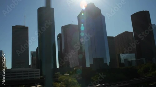 One of the backlit skyscrapers of downtown Houston as viewed from the intrastate highway catches a ray of light and reflects it back in a sun flare that travels along with the scene. photo